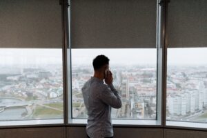 Businessman standing by window, making a phone call with city view.