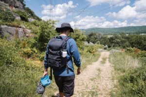 A hiker with a backpack walking down a forest trail under a sunny sky.
